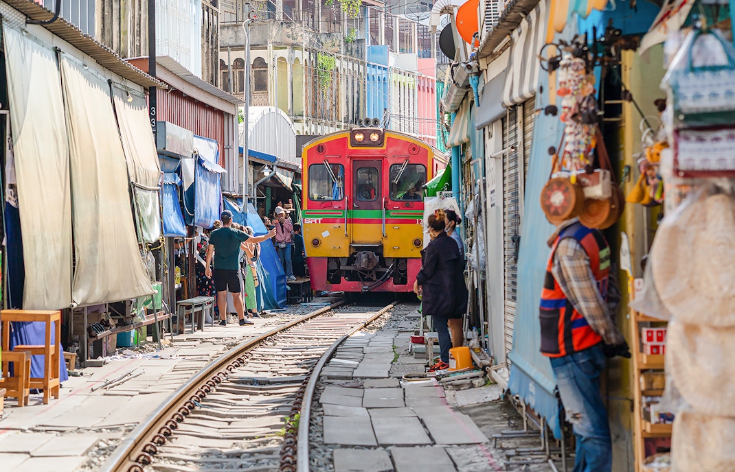 Train passing through Maeklong Railway Market with tourists and vendors nearby.