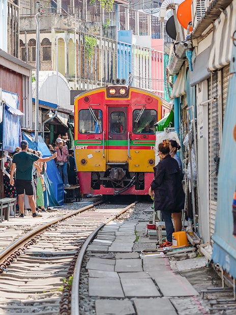 Train passing through Maeklong Railway Market with tourists and vendors nearby.