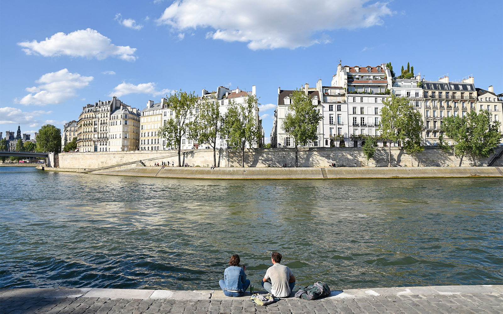 Île Saint-Louis Paris, view of historic buildings along the Seine River with a bridge in the background.