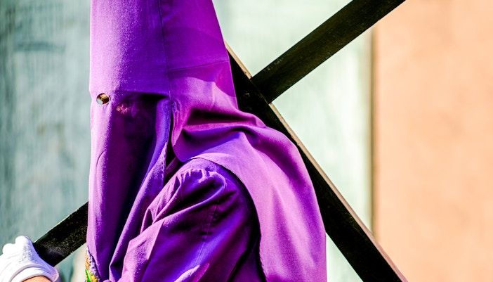 Nazareno carrying a cross in a hooded robe during Good Friday procession, Paris.