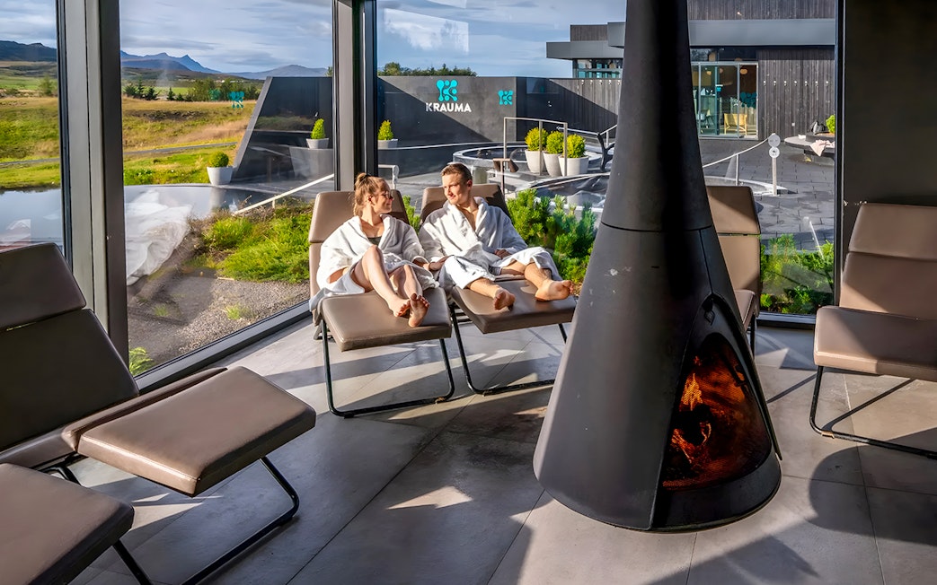 Couple relaxing in robes by a fireplace at Krauma Geothermal Baths, Iceland.