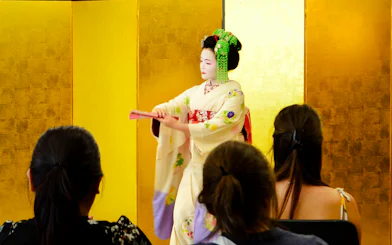 Maiko performs traditional dance with a fan for an audience in Kyoto, Japan.