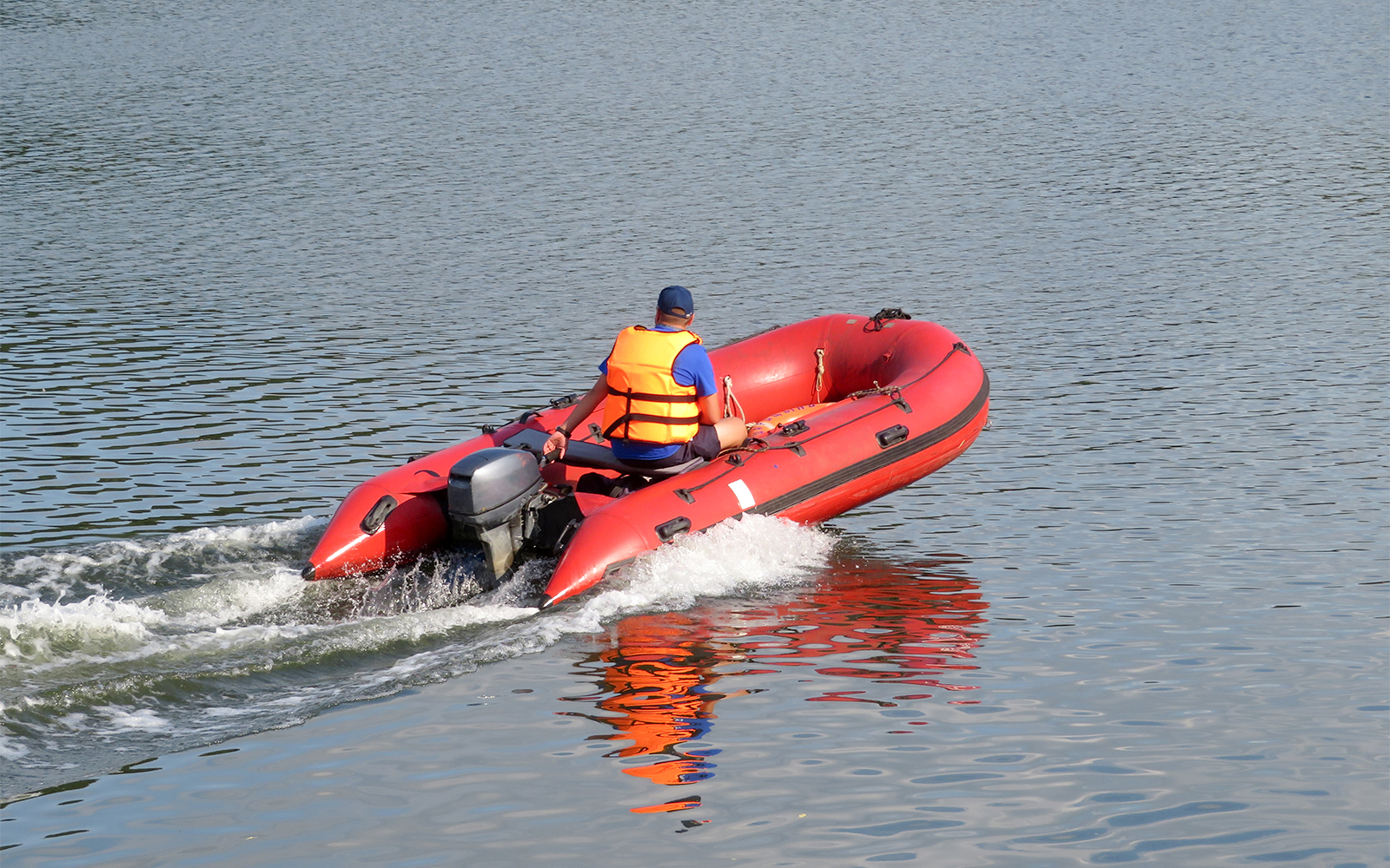 Lifeguard in life jacket operating a red rescue boat on a calm lake.