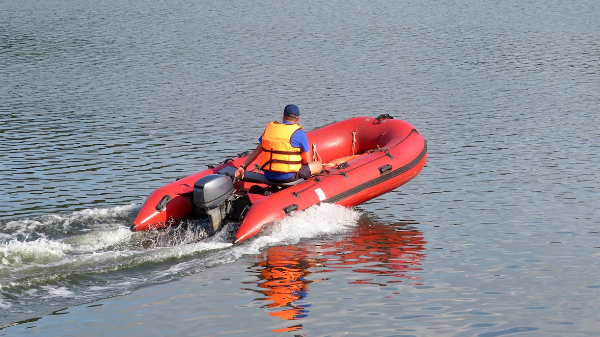 Lifeguard in life jacket operating a red rescue boat on a calm lake.