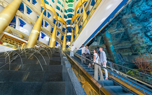 Guests on escalator inside Burj Al Arab, Dubai, with gold columns and aquarium view.