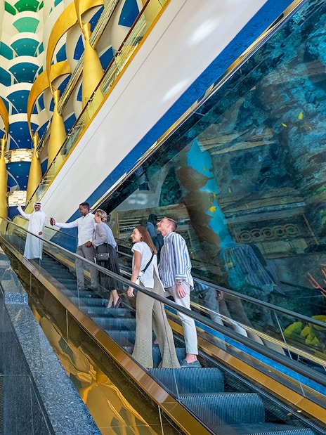 Guests on escalator inside Burj Al Arab, Dubai, with gold columns and aquarium view.