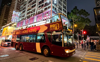 Big Bus Tours double-decker in Hong Kong at night with city lights and passengers on board.