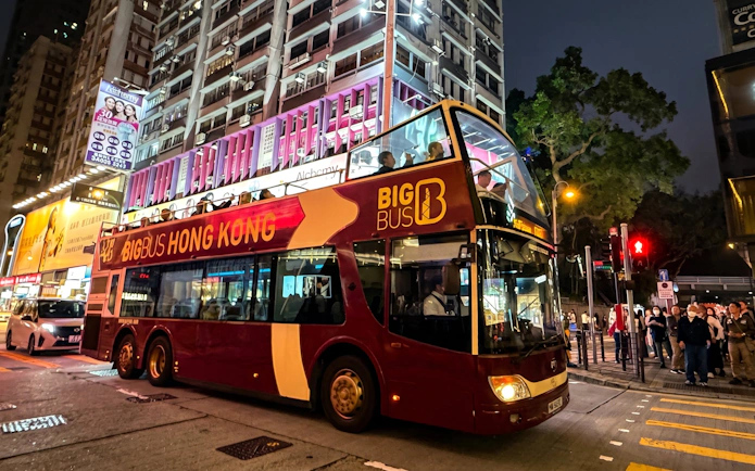 Big Bus Tours double-decker in Hong Kong at night with city lights and passengers on board.