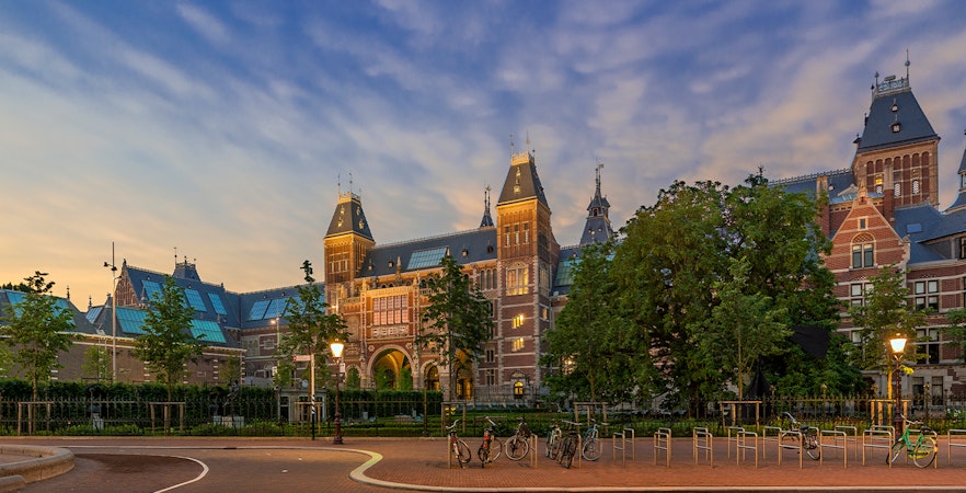 Rijksmuseum exterior with bicycles in Amsterdam at sunset.
