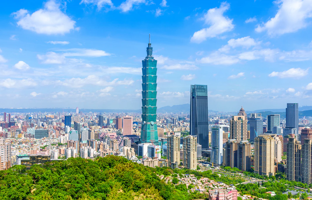 Taipei 101 towering over Taipei cityscape with lush greenery in the foreground.