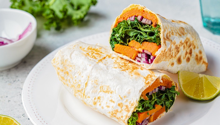 Sweet potato burrito wrap with fresh ingredients on a wooden table.