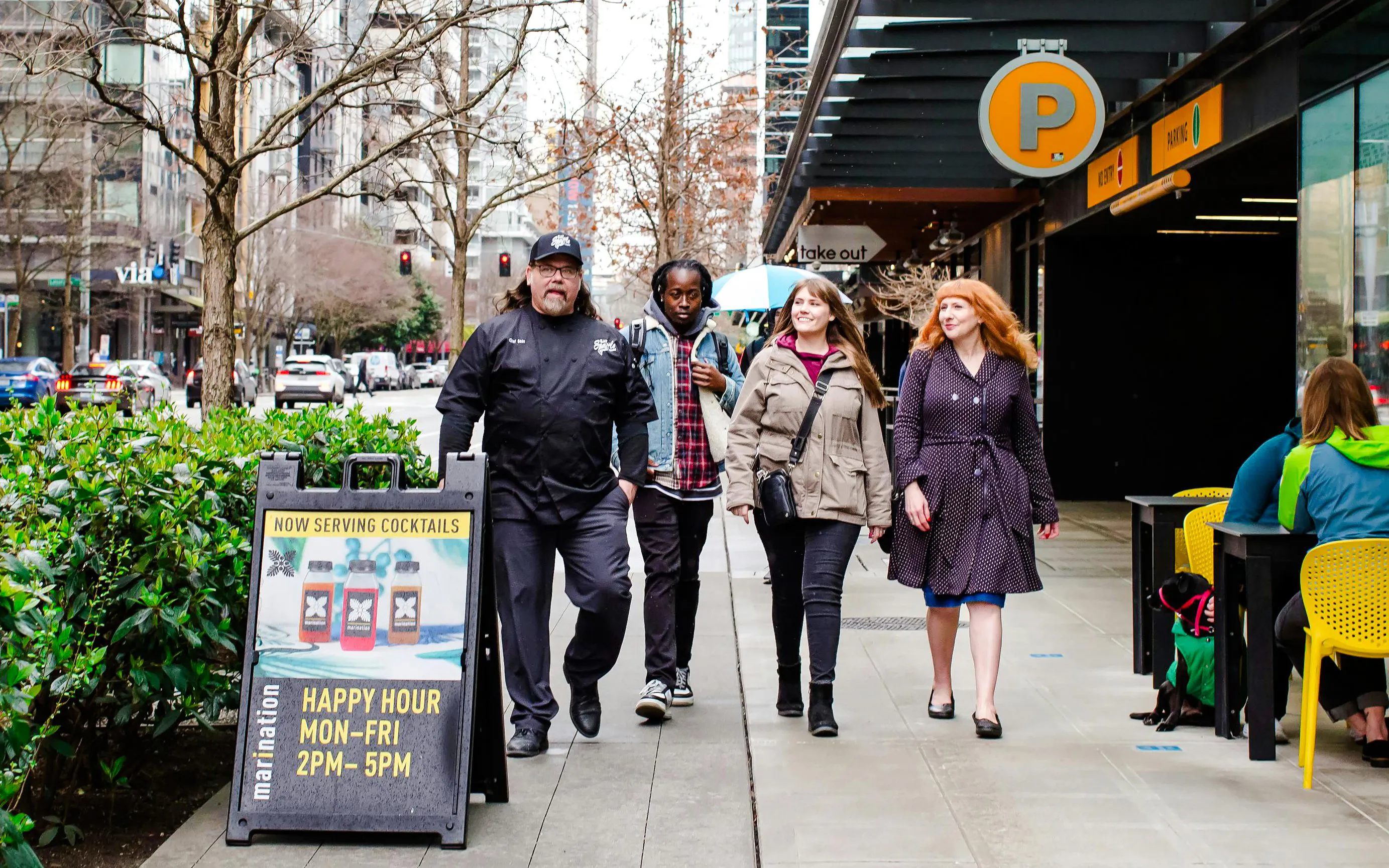 Group walking past a Seattle happy hour sign on a city street.