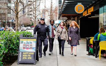 Group walking past a Seattle happy hour sign on a city street.
