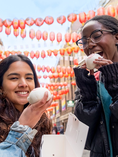 Tourists enjoying bao buns under lanterns in London's Soho on a food tour.