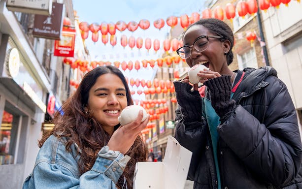 Tourists enjoying bao buns under lanterns in London's Soho on a food tour.