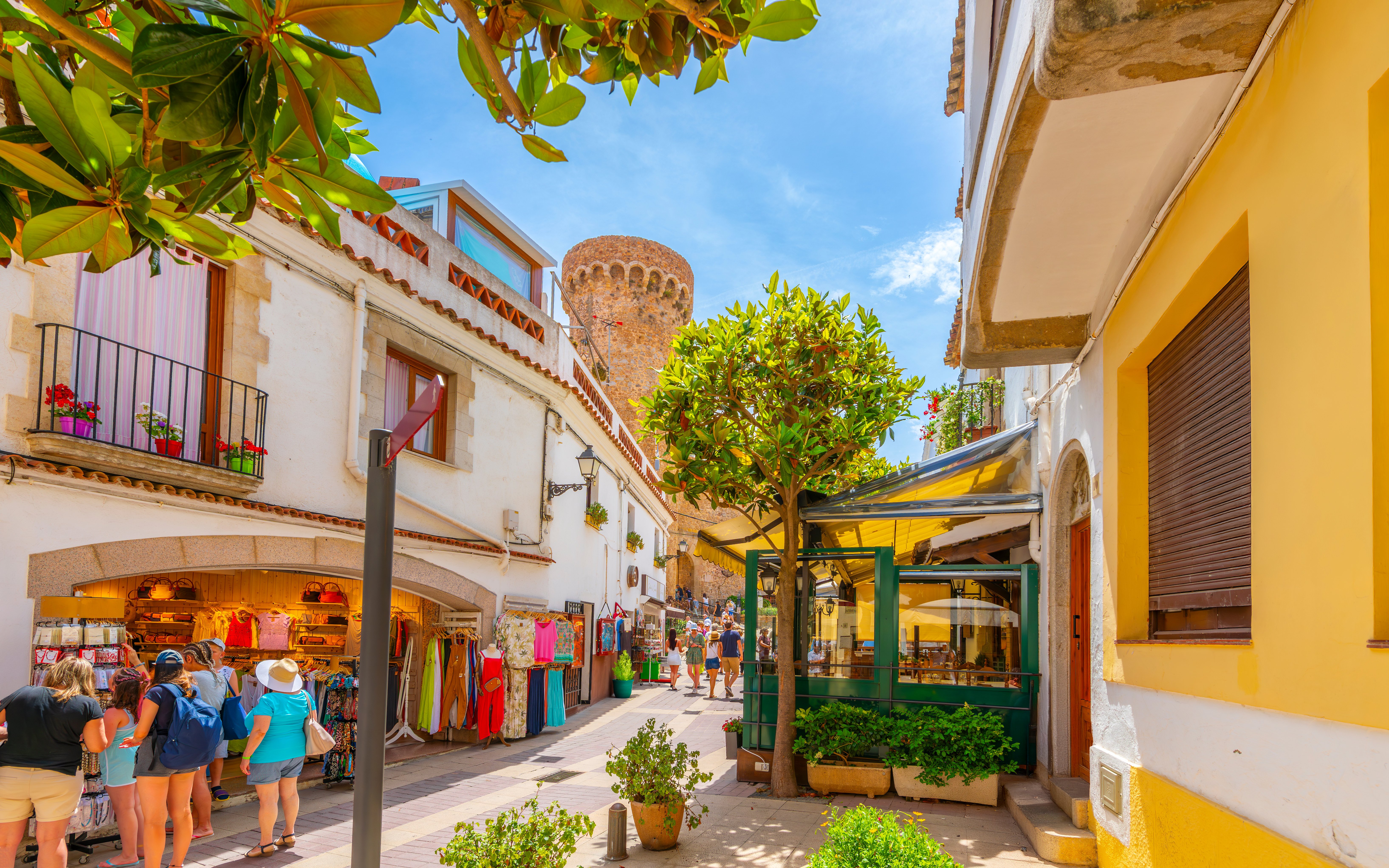 Narrow street with shops and cafes in Tossa de Mar's whitewashed old town, Costa Brava, Spain.