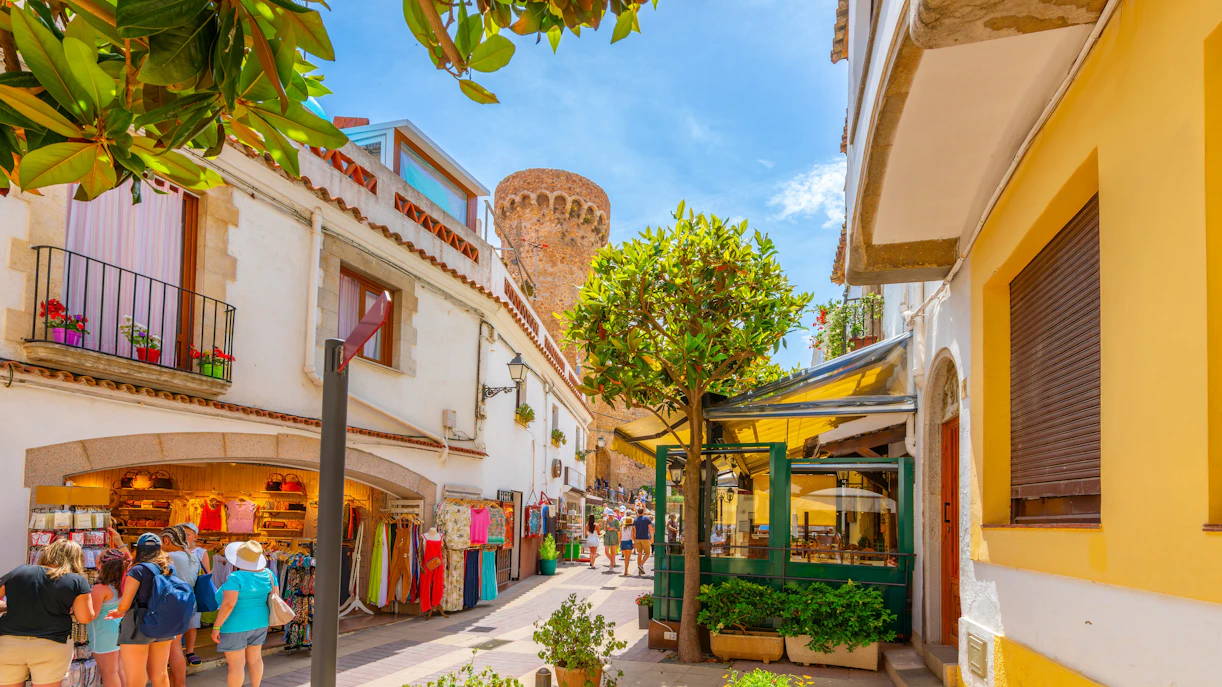 Narrow street with shops and cafes in Tossa de Mar's whitewashed old town, Costa Brava, Spain.