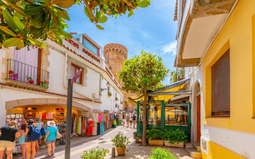 Narrow street with shops and cafes in Tossa de Mar's whitewashed old town, Costa Brava, Spain.