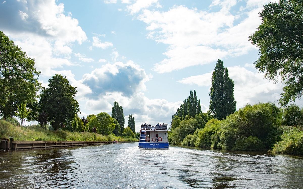 Sightseeing cruise boat on River Ouse in York surrounded by lush greenery.