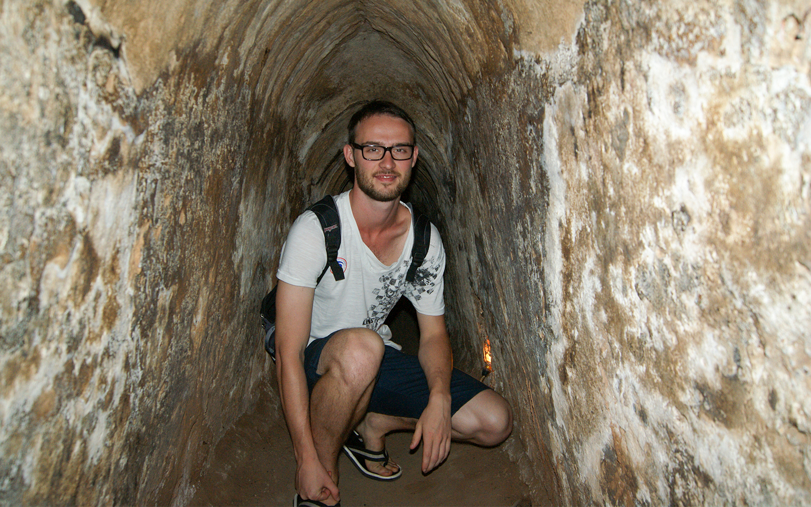 Young tourist crouching inside narrow Cu Chi tunnel in Vietnam.