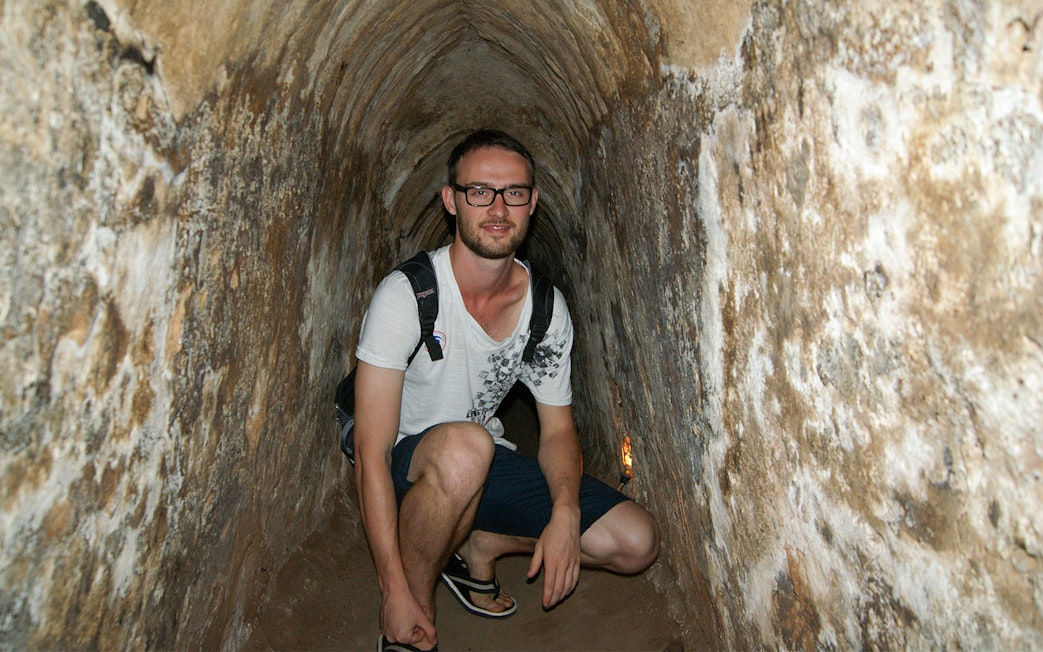 Young tourist crouching inside narrow Cu Chi tunnel in Vietnam.