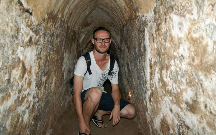 Young tourist crouching inside narrow Cu Chi tunnel in Vietnam.