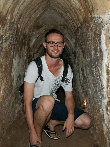 Young tourist crouching inside narrow Cu Chi tunnel in Vietnam.