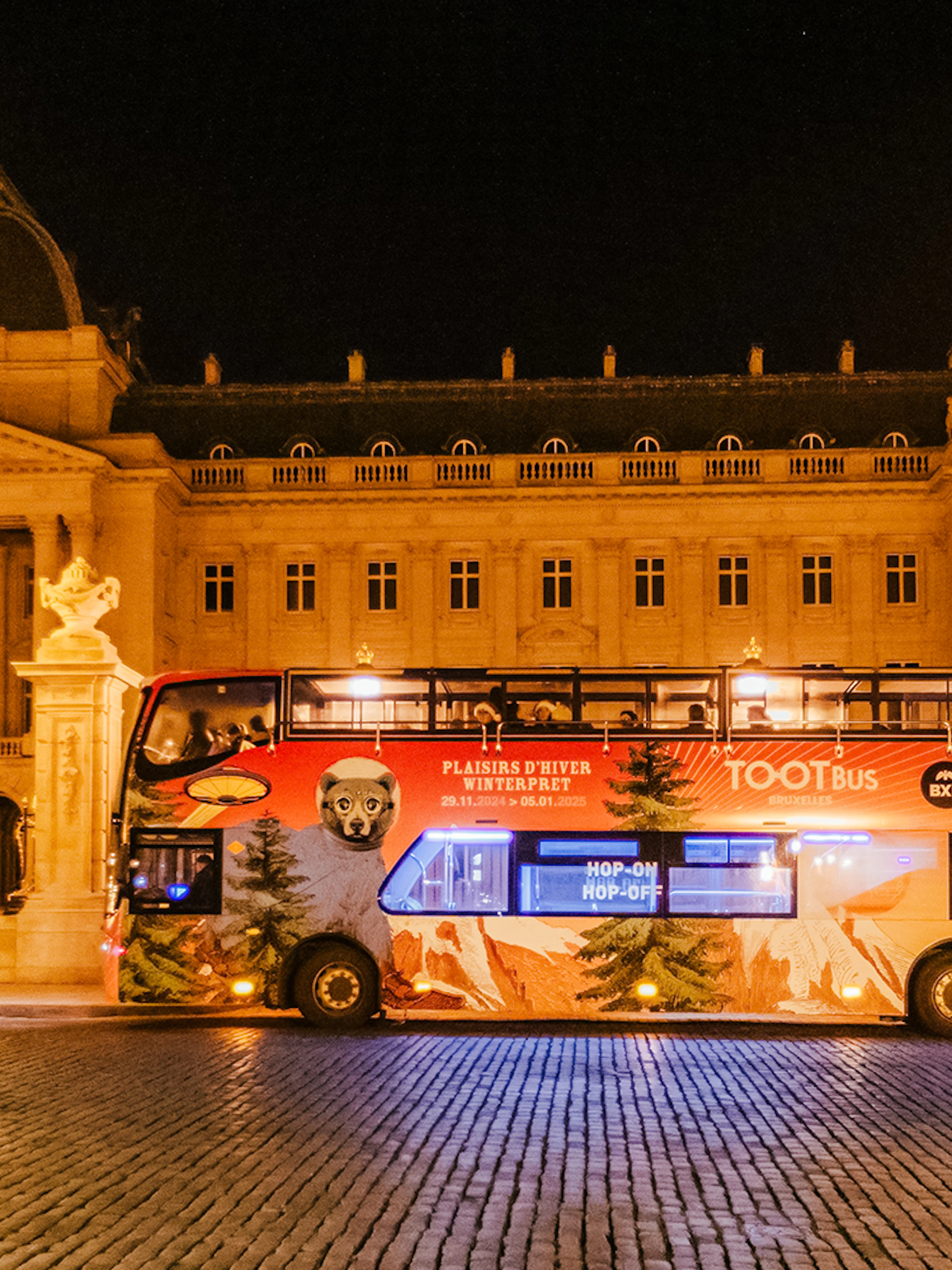 Brussels hop-on hop-off bus at night near a historic building during Christmas season.