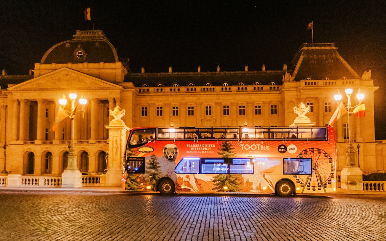 Brussels hop-on hop-off bus at night near a historic building during Christmas season.