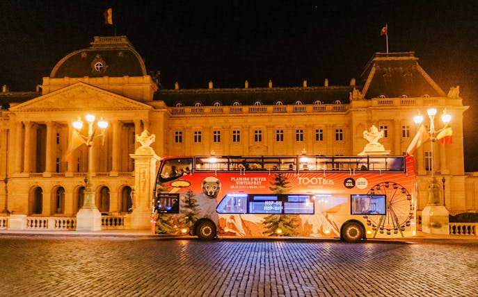 Brussels hop-on hop-off bus at night near a historic building during Christmas season.