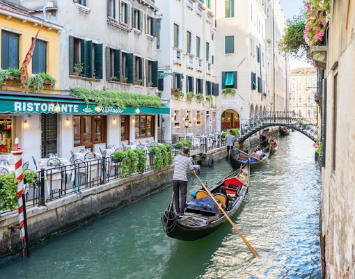 Gondolas on a canal in Venice, Italy, with historic buildings in the background.