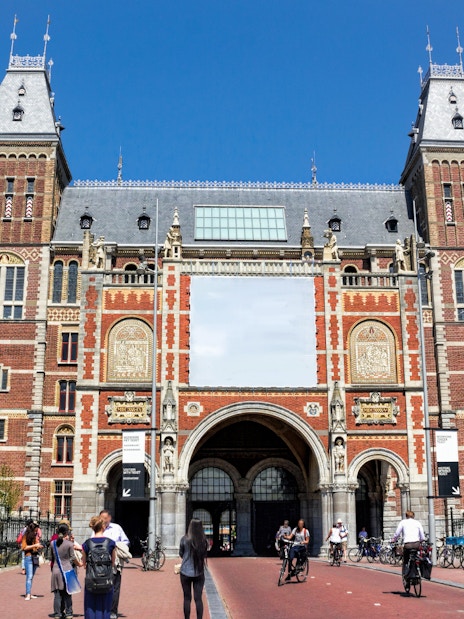 Rijksmuseum entrance with cyclists and visitors in Amsterdam.