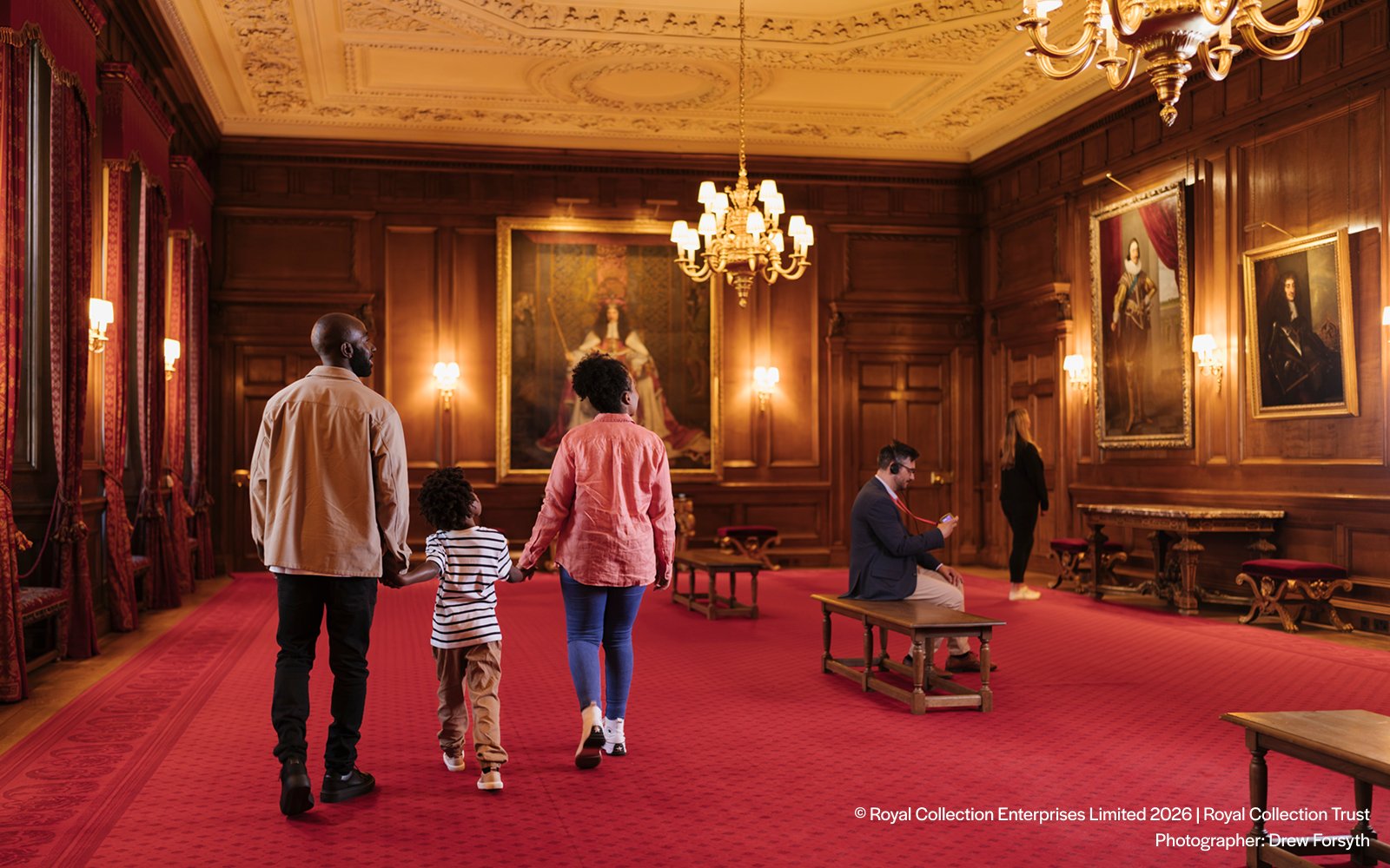 Visitors exploring the ornate interior of the Palace of Holyroodhouse with portraits on the walls.