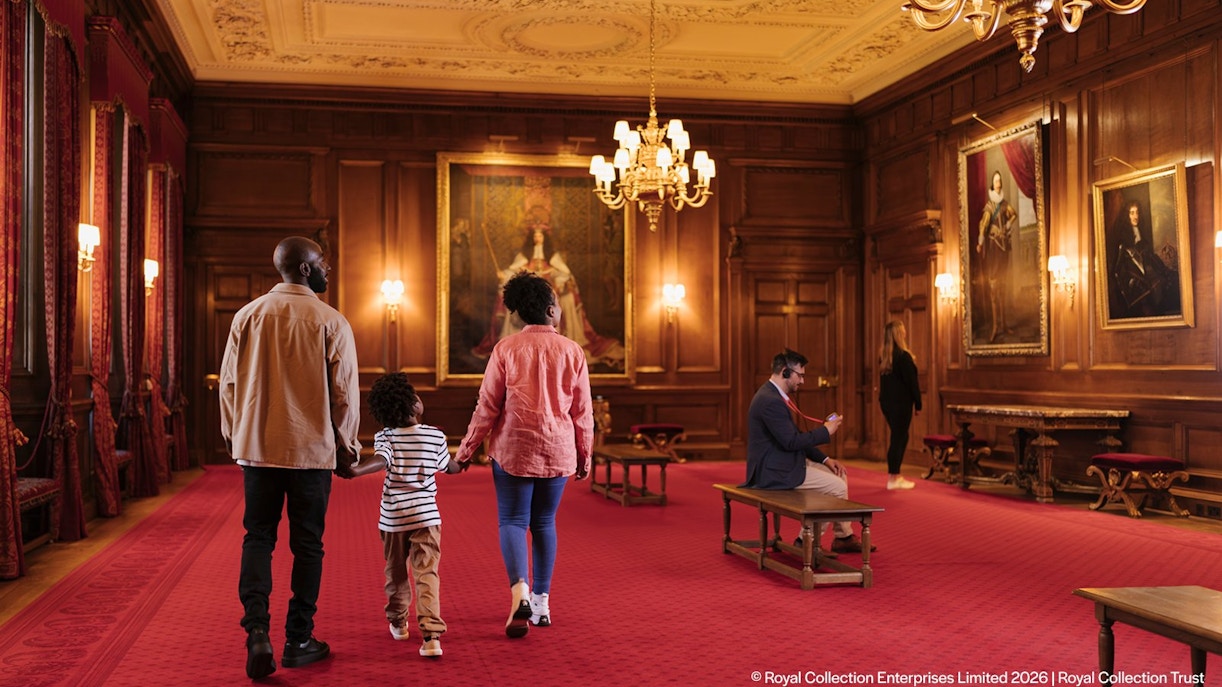 Visitors exploring the ornate interior of the Palace of Holyroodhouse with portraits on the walls.