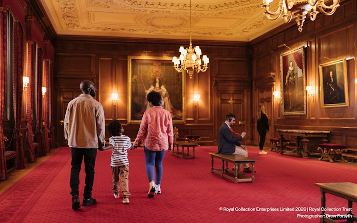 Visitors exploring the ornate interior of the Palace of Holyroodhouse with portraits on the walls.