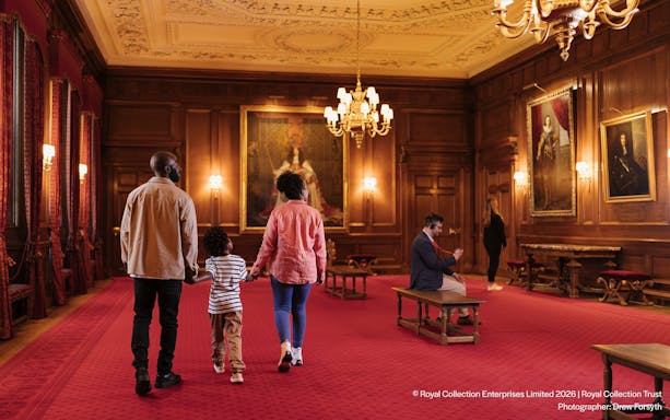 Visitors exploring the ornate interior of the Palace of Holyroodhouse with portraits on the walls.