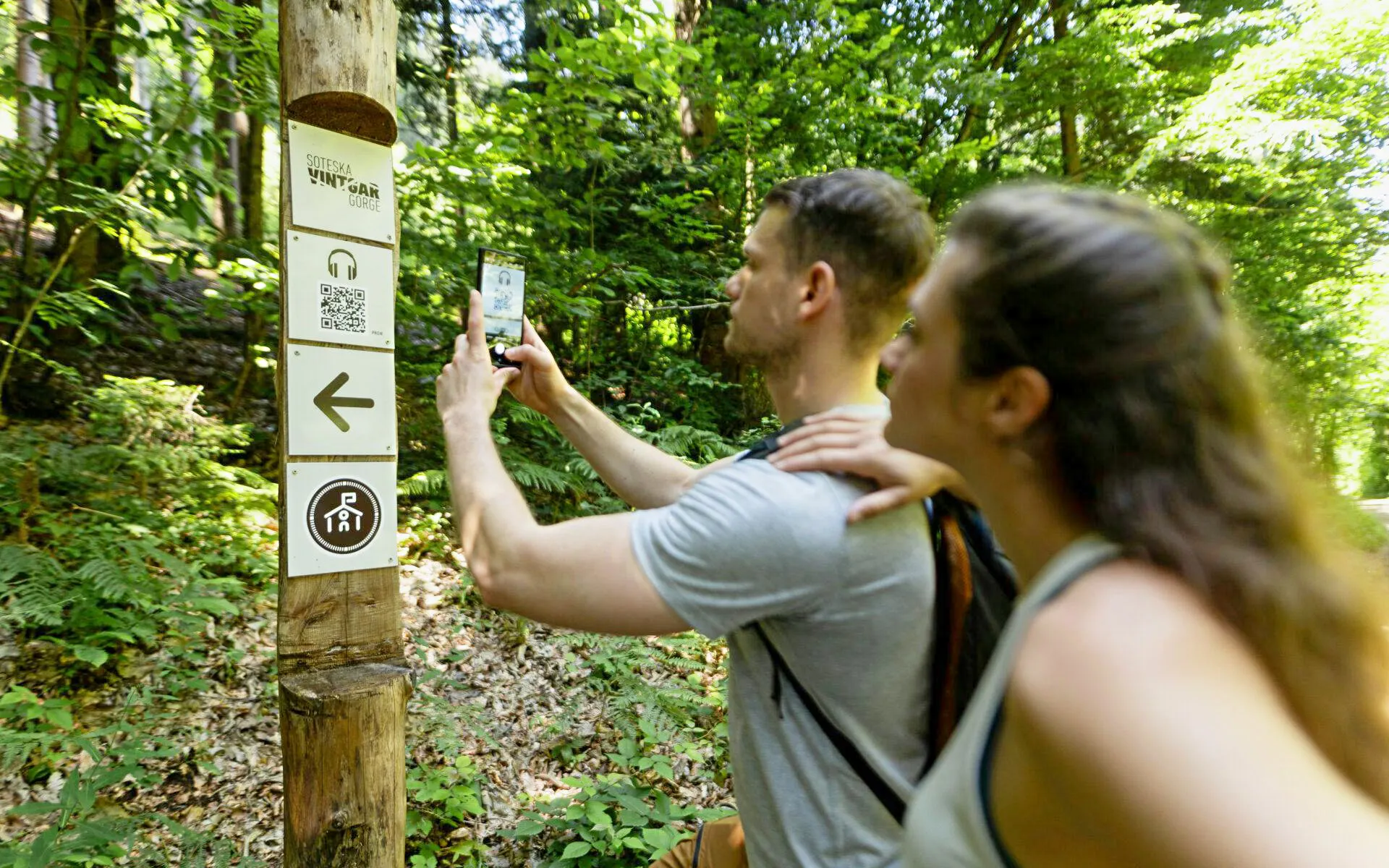 Visitors using an audio guide app at Vintgar Gorge trail sign, Slovenia.