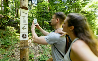Visitors using an audio guide app at Vintgar Gorge trail sign, Slovenia.