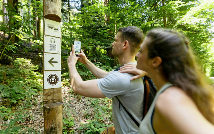 Visitors using an audio guide app at Vintgar Gorge trail sign, Slovenia.