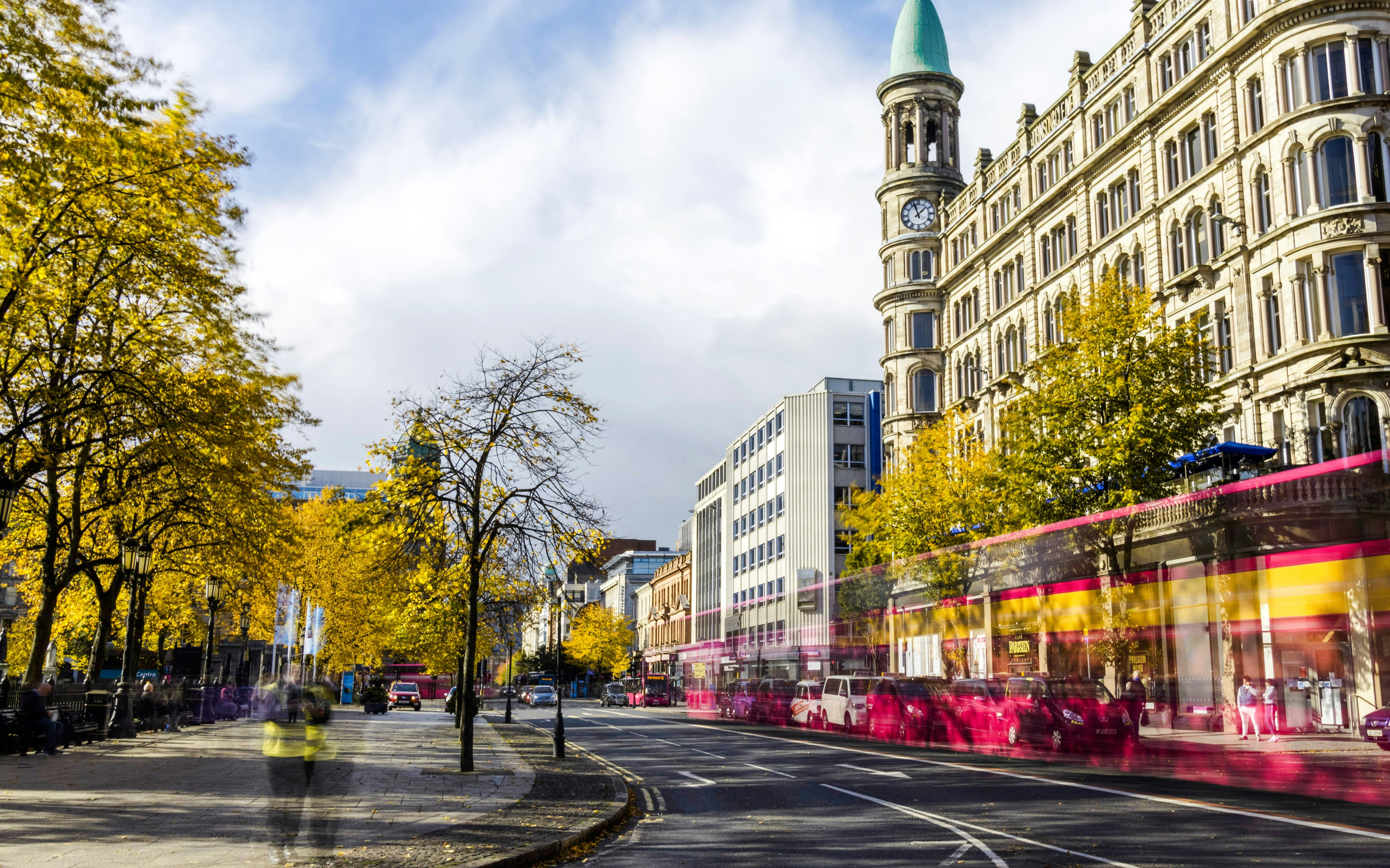 Historic building and autumn trees along a busy street in Belfast city centre.