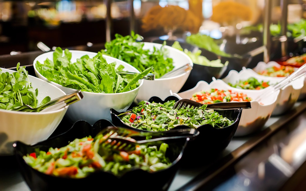 Salad buffet with various greens and vegetables in bowls.