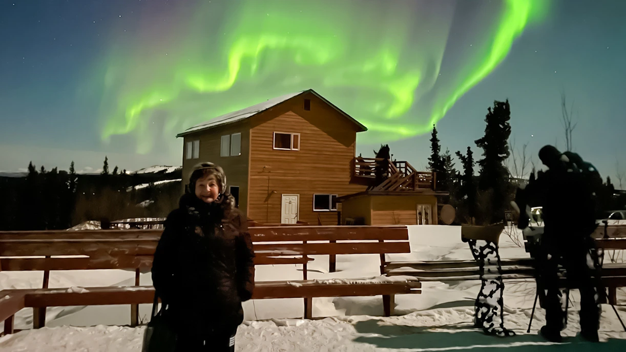 Aurora Borealis over lodge with people viewing Northern Lights in Alaska.