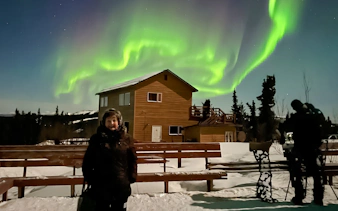Aurora Borealis over lodge with people viewing Northern Lights in Alaska.
