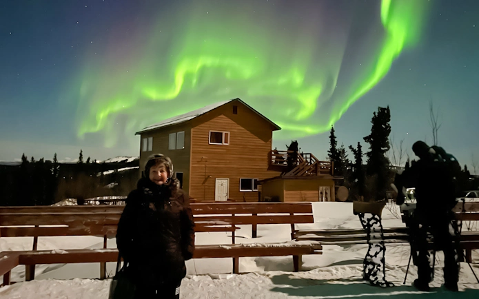Aurora Borealis over lodge with people viewing Northern Lights in Alaska.