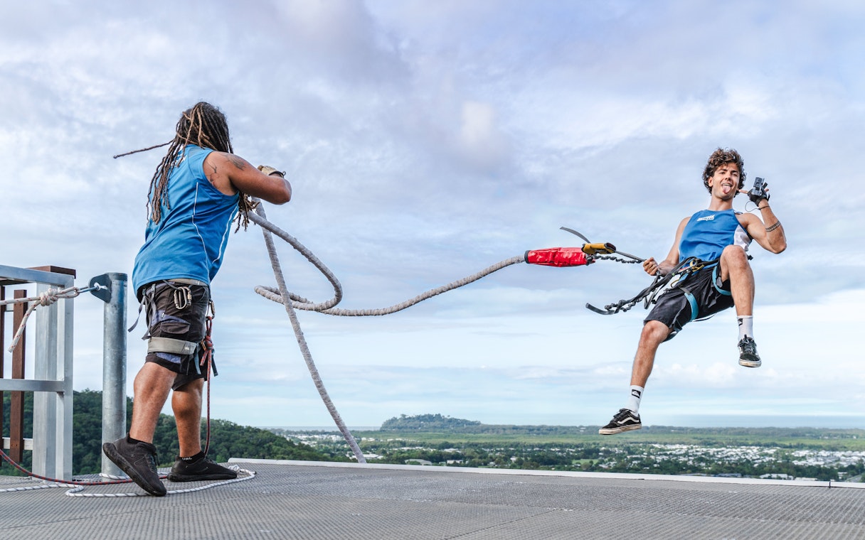 Person harnessed for Walk The Plank by AJ Hackett, Cairns, with scenic view in background.