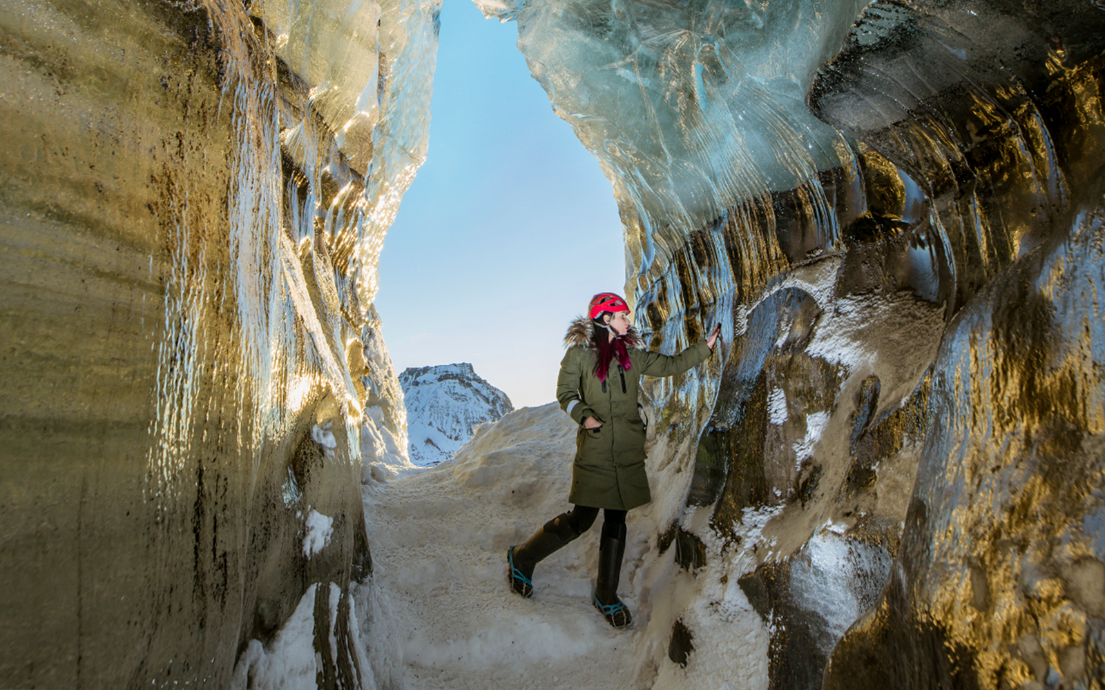 Guest exploring inside Katla Ice Cave with icy walls and snowy path, Iceland.
