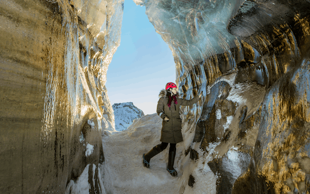 Guest exploring inside Katla Ice Cave with icy walls and snowy path, Iceland.