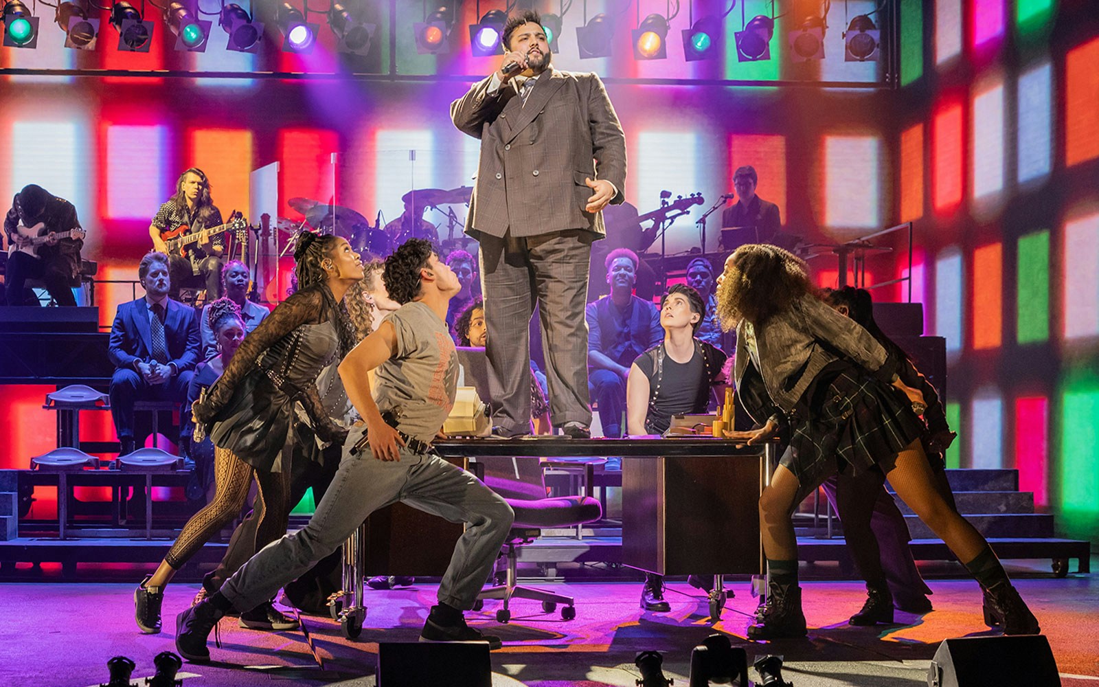 Performer singing on stage at "Just for One Day" with dancers and colorful lights.