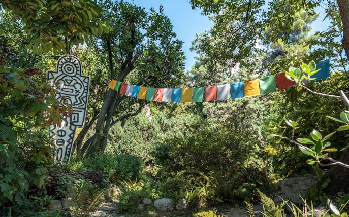 Colorful flags and abstract sculpture in lush ANIMA Garden, Marrakech.