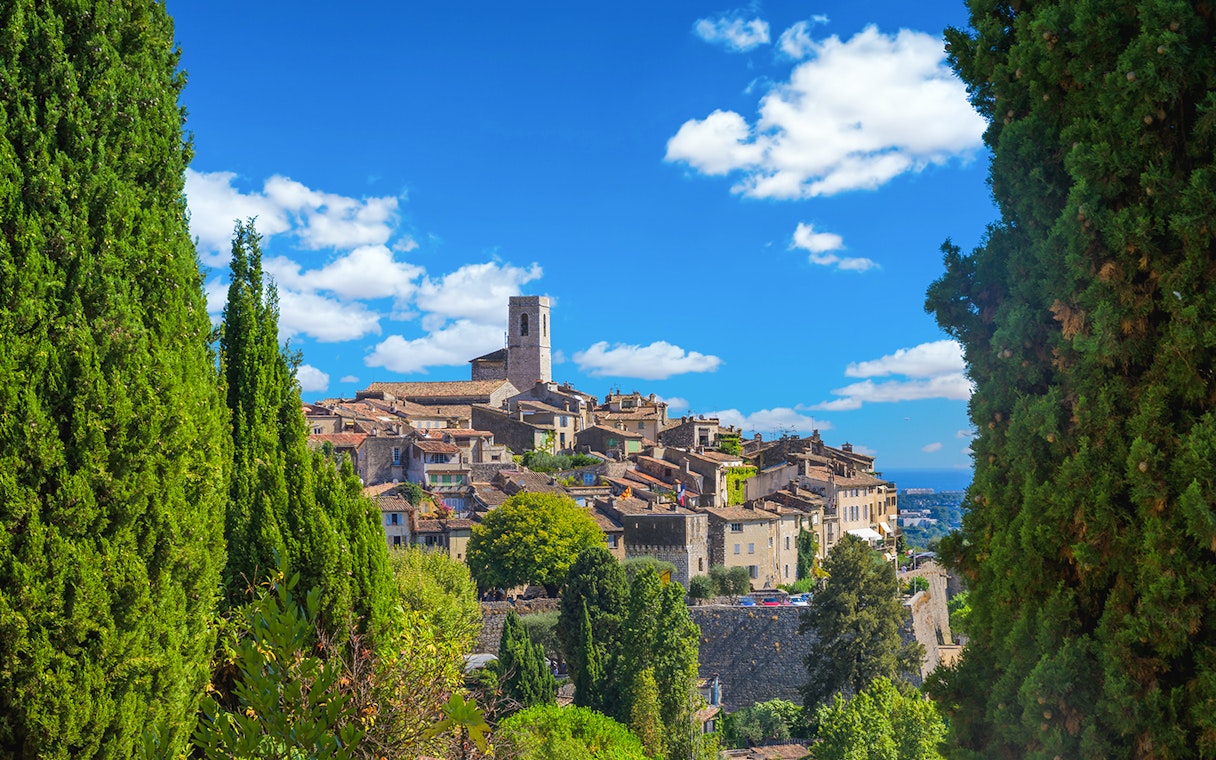 Hilltop village in the French Riviera with stone buildings and a church tower, surrounded by greenery.